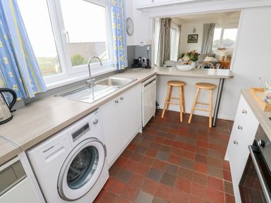 A kitchen with washing machine dishwasher sink and breakfast bar with two wooden stools at Valley High in Solva