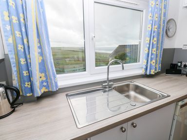 A kitchen sink under a window with blue and yellow curtains and a kettle on the countertop at Valley High in Solva