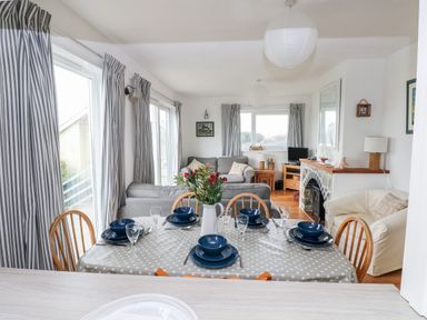 A dining table set with blue plates and glasses next to a living area with sofas and a fireplace at Valley High in Solva