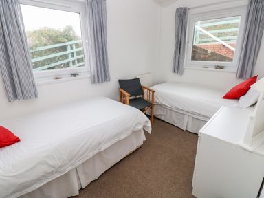 A bedroom with two single beds a black chair and a white dresser at Valley High in Solva