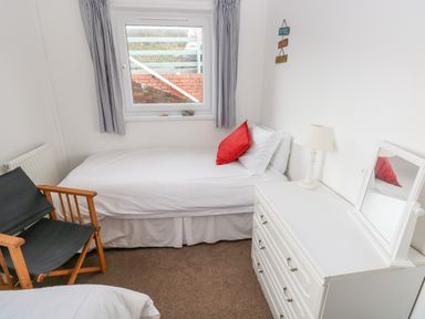 A small bedroom with a single bed with white bedding and a red pillow a wooden chair a white dresser with a lamp and a mirror and a window with curtains at Valley High in Solva