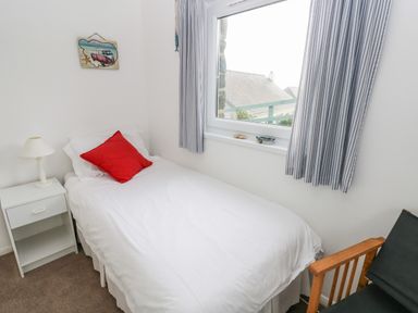 A small bedroom with a single bed with white bedding and a red pillow next to a window with striped curtains at Valley High in Solva