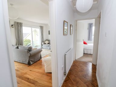 A hallway leading to a living room with sofas and a bedroom with a bed and curtains at Valley High in Solva