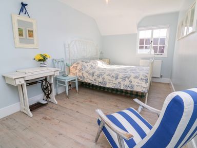 A bedroom with a bed a striped armchair a vintage sewing table and a window at 3 Elm Cottage in Carhampton