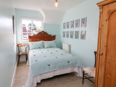 A bedroom with a bed with floral bedding two wooden chairs a wooden wardrobe and framed pictures on the wall at 3 Elm Cottage in Carhampton