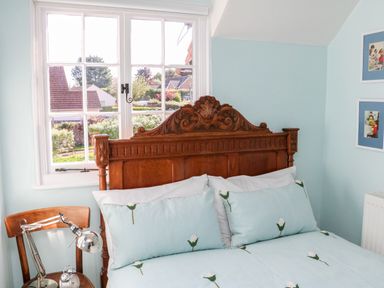 A bedroom with a wooden carved headboard a chair with a lamp and an alarm clock next to a window at 3 Elm Cottage in Carhampton