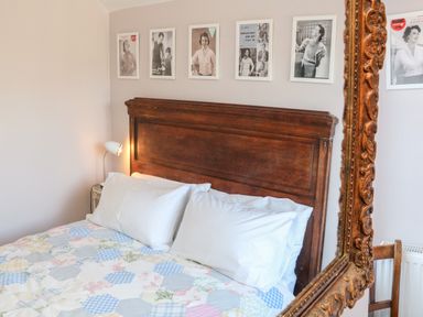 A bedroom with a wooden bed headboard white pillows a patchwork quilt and framed pictures on the wall at 3 Elm Cottage in Carhampton