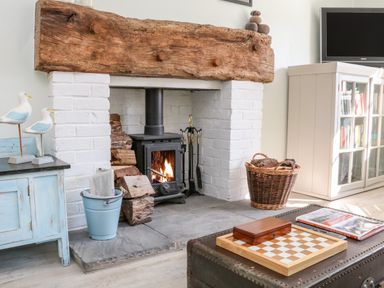 A fireplace with a wood stove surrounded by logs and tools next to a blue cabinet and a white bookshelf at 3 Elm Cottage in Carhampton