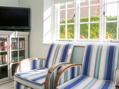 Two striped armchairs near a window and a cabinet with books and a television at 3 Elm Cottage in Carhampton