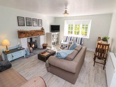 A living room with a fireplace a sofa striped armchairs a television and a small dining table at 3 Elm Cottage in Carhampton