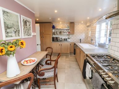 A kitchen with wooden cabinets a countertop with a sink a stove and a wooden dining table with chairs and sunflowers at 3 Elm Cottage in Carhampton