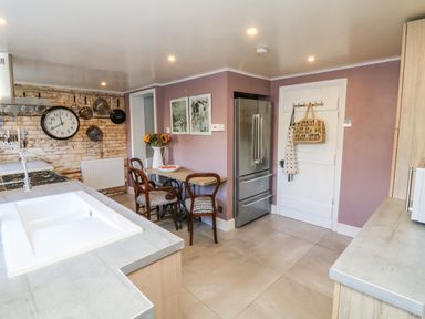 A kitchen with a large sink countertop a dining table with chairs a refrigerator and pots hanging on a brick wall at 3 Elm Cottage in Carhampton
