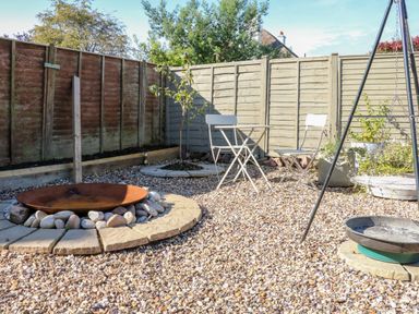 A gravel garden with a fire pit surrounded by stones a small table with two chairs and a swing at 3 Elm Cottage in Carhampton