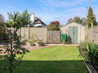 A fenced backyard with a lawn a garden shed a wheelbarrow and potted plants at 3 Elm Cottage in Carhampton