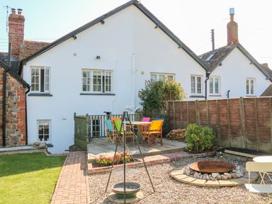 A garden with a wooden deck and colorful chairs outside a white house at 3 Elm Cottage in Carhampton