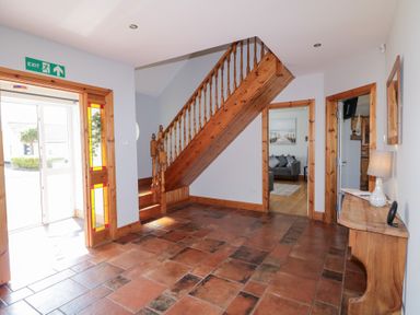 A hallway with tiled floor wooden staircase and a wooden console table with a lamp at SeaShells in Castlerock