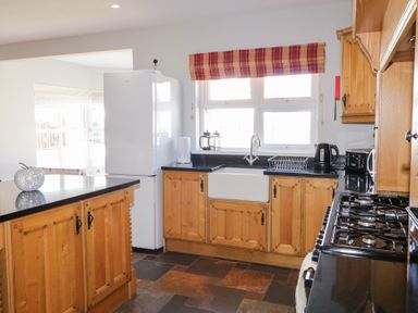 A kitchen with wooden cabinets a white refrigerator a stove a sink and a window with a red and orange striped blind at SeaShells in Castlerock