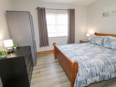 A bedroom with a wooden bed blue and white bedspread a black dresser a gray wardrobe and two lamps at SeaShells in Castlerock
