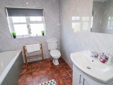 A bathroom with a bathtub a toilet a sink with toiletries a towel rack and a window with plants at SeaShells in Castlerock