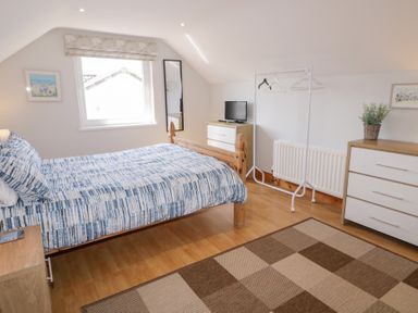 A bedroom with a wooden bed with blue patterned bedding a window a small TV on a chest of drawers a clothes rack and a larger dresser in SeaShells Castlerock