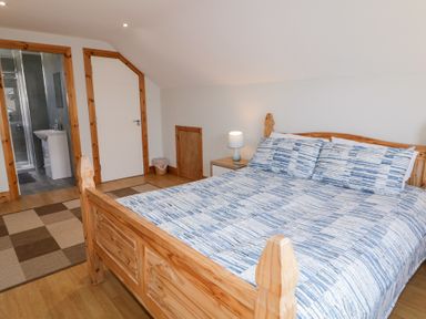 A bedroom with a wooden bed and blue patterned bedding next to a nightstand with a lamp and an adjoining bathroom at SeaShells in Castlerock