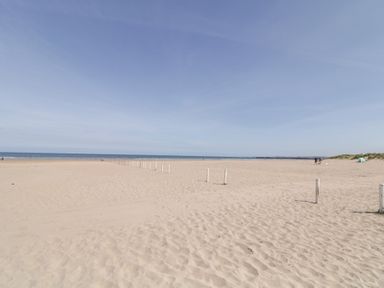 A sandy beach with white posts leading to the sea and a few people near sand dunes at SeaShells in Castlerock