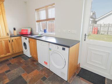 A utility room with washing machine dishwasher dryer wooden cabinets and a door leading outside at SeaShells in Castlerock