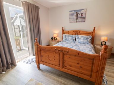 A bedroom with a wooden bed frame two side tables with lamps a painting above the bed and an open door with curtains at SeaShells in Castlerock