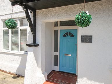 Front entrance with a blue door and hanging green decorations at The White Cottage in Weymouth