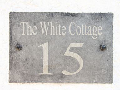 A house number plaque with the text The White Cottage 15 on a white wall at The White Cottage in Weymouth