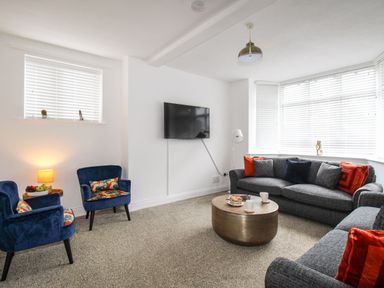 A living room with gray sofas and blue armchairs with floral cushions at The White Cottage in Weymouth