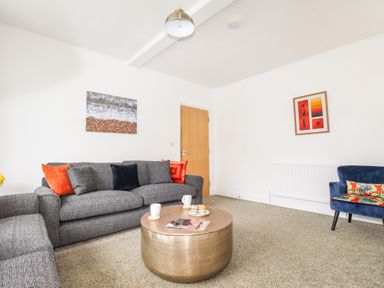 A living room with gray sofas a round coffee table and a blue chair at The White Cottage in Weymouth