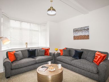 A living room with two grey sofas and orange and black cushions at The White Cottage in Weymouth
