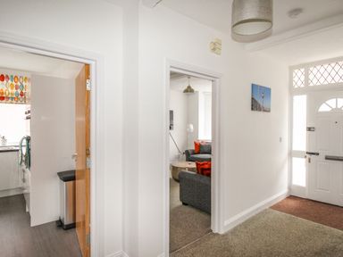 A hallway with doorways leading to a kitchen and a living room with a white front door at The White Cottage in Weymouth