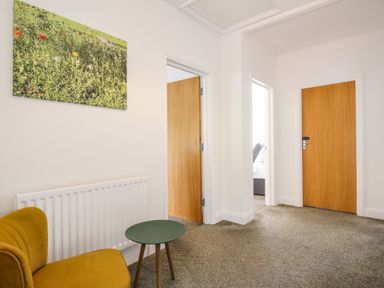 A hallway with three wooden doors a yellow chair a small round table a radiator and a wall picture at The White Cottage in Weymouth