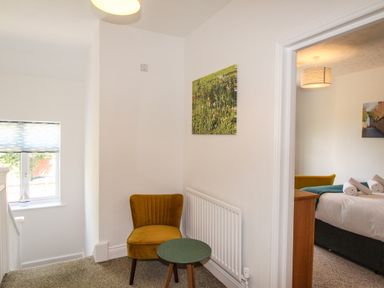 A small seating area with a mustard chair and round table next to a radiator with a bedroom visible through a door at The White Cottage in Weymouth