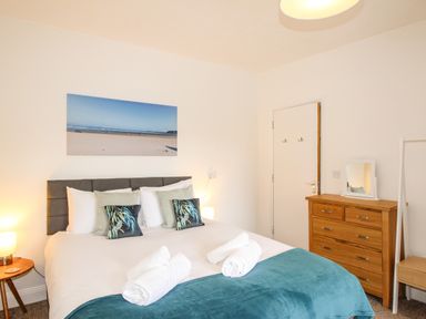 A bedroom with a bed with rolled towels bedside tables a wooden chest of drawers and a mirror at The White Cottage in Weymouth