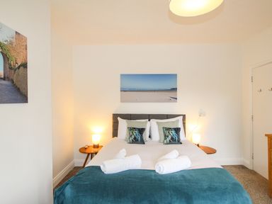 A bedroom with a double bed two bedside tables with lamps and beach photos on the walls at The White Cottage in Weymouth