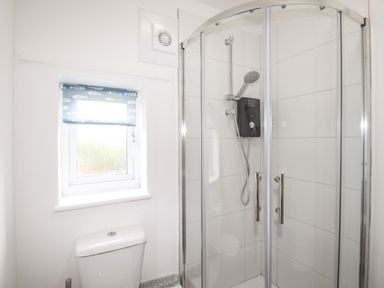 A bathroom with a shower cabin a toilet and a small window with a fish pattern blind at The White Cottage in Weymouth
