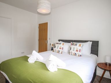 A bedroom with a double bed with white bedding green blanket and decorative pillows next to a wooden door at The White Cottage in Weymouth