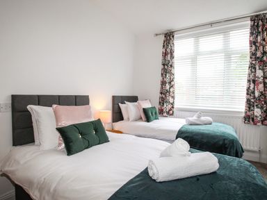 A bedroom with two single beds with green and pink pillows and floral curtains at The White Cottage in Weymouth