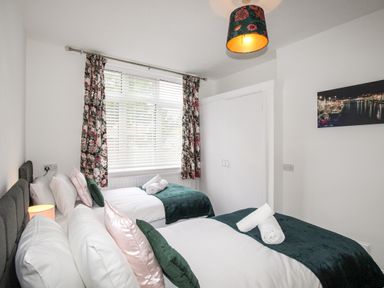 A bedroom with two single beds with rolled towels on the blankets a window with floral curtains and a closet at The White Cottage in Weymouth