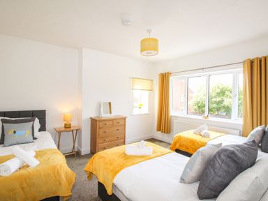 A bedroom with three single beds yellow blankets dresser and window curtains at The White Cottage in Weymouth