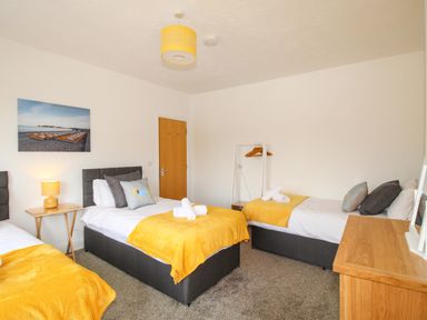 A bedroom with three single beds yellow blankets and a wooden dresser at The White Cottage in Weymouth