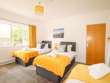 A bedroom with three single beds each covered with yellow blankets and white towels on a carpet floor at The White Cottage in Weymouth