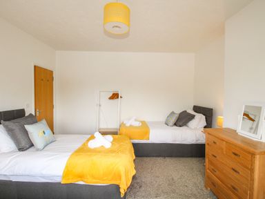 A bedroom with two beds with yellow throws a wooden dresser and a clothing rack at The White Cottage in Weymouth