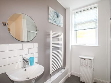 A bathroom with a white pedestal sink mirror towel radiator and window with blind at The White Cottage in Weymouth