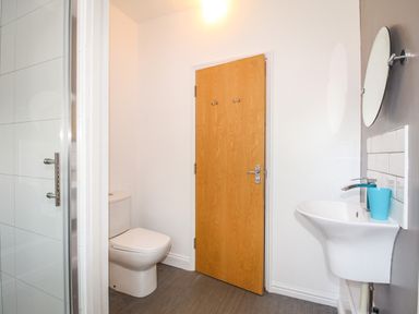 A bathroom with a toilet sink a round mirror and a wooden door at The White Cottage in Weymouth