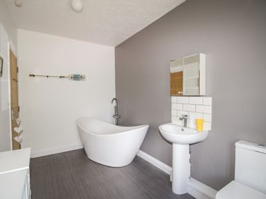 A bathroom with a freestanding bathtub, pedestal sink, wall cabinet, and toilet at The White Cottage in Weymouth