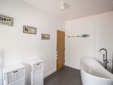 A bathroom with a freestanding bathtub wooden door two white storage units and wall decorations at The White Cottage in Weymouth